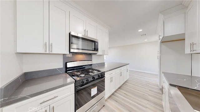 kitchen with white cabinets, black gas range oven, stainless steel microwave, light wood-style floors, and recessed lighting