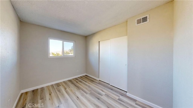 unfurnished bedroom featuring baseboards, a textured ceiling, and light wood finished floors