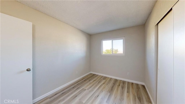 unfurnished bedroom with light wood-style flooring, a closet, baseboards, and a textured ceiling