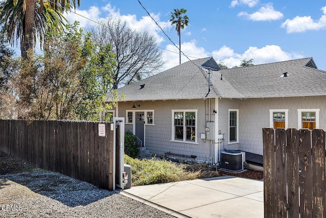 rear view of house with central AC, roof with shingles, and fence