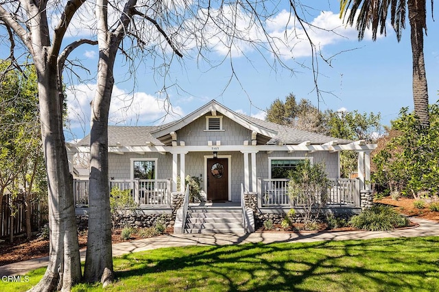 view of front of property featuring covered porch, a front lawn, and a shingled roof