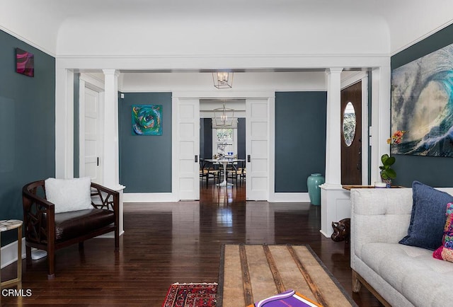 living area featuring ornate columns, a notable chandelier, baseboards, and wood finished floors