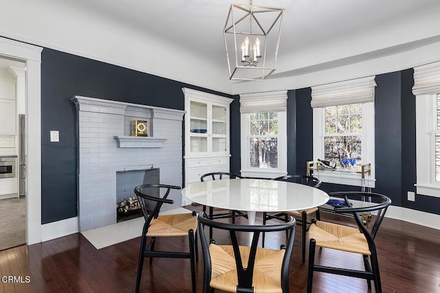 dining space with hardwood / wood-style flooring, a fireplace with flush hearth, a chandelier, and baseboards