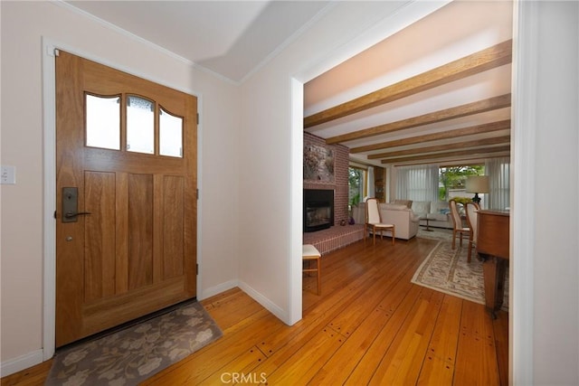 foyer entrance featuring a fireplace, ornamental molding, light wood-type flooring, beamed ceiling, and baseboards