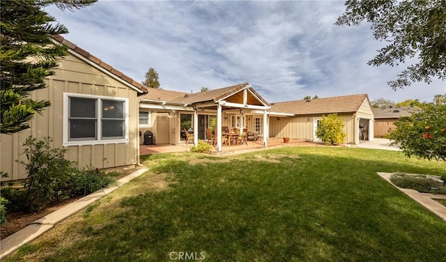 rear view of house with board and batten siding, a patio area, a yard, and a tiled roof