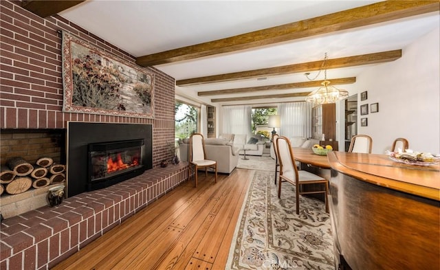 dining space with beamed ceiling, a fireplace, wood-type flooring, and a notable chandelier