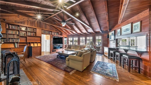 living area with lofted ceiling with beams, ceiling fan, wooden ceiling, wood walls, and wood-type flooring