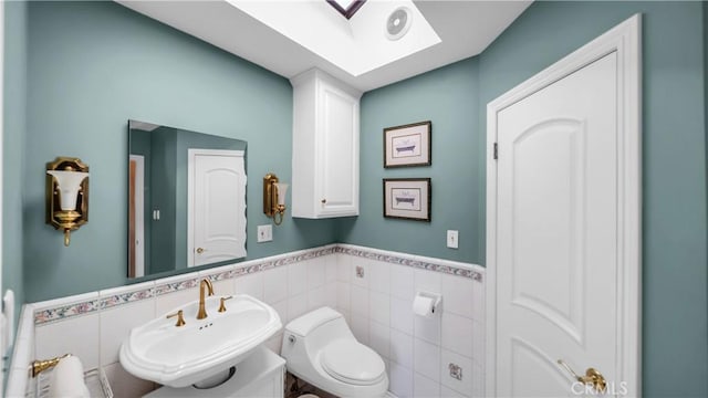 bathroom with toilet, a wainscoted wall, a skylight, a sink, and tile walls