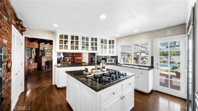 kitchen featuring wallpapered walls, a kitchen island, glass insert cabinets, stainless steel microwave, and black gas stovetop