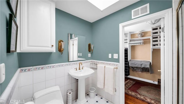 bathroom with a skylight, visible vents, wainscoting, toilet, and tile walls