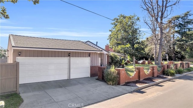 view of front facade featuring concrete driveway, a chimney, a tile roof, and fence