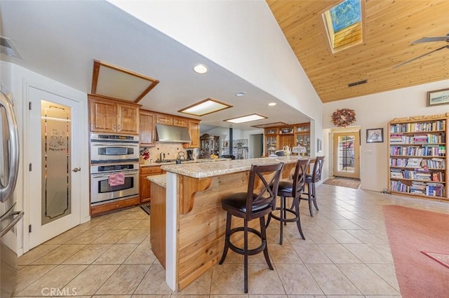 45544 Pine River Rd, Ahwahnee, CA 93601 - kitchen featuring light tile patterned floors, a kitchen breakfast bar, stainless steel double oven, and exhaust hood