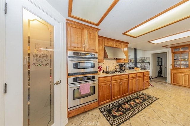 45544 Pine River Rd, Ahwahnee, CA 93601 - kitchen with light tile patterned floors, tasteful backsplash, brown cabinets, stainless steel appliances, and under cabinet range hood