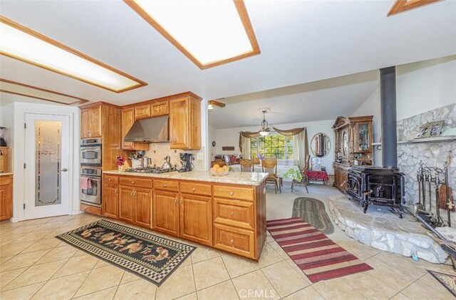45544 Pine River Rd, Ahwahnee, CA 93601 - kitchen with light tile patterned floors, under cabinet range hood, stainless steel appliances, vaulted ceiling, and a wood stove