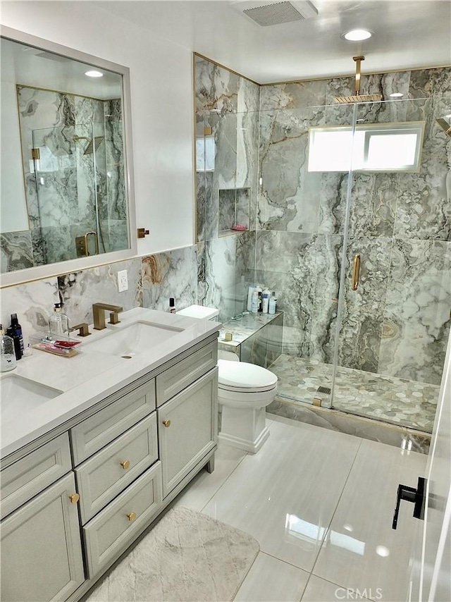 full bathroom featuring toilet, a sink, visible vents, a marble finish shower, and double vanity