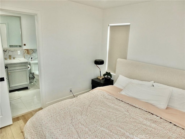 bedroom with light wood finished floors, baseboards, and a sink