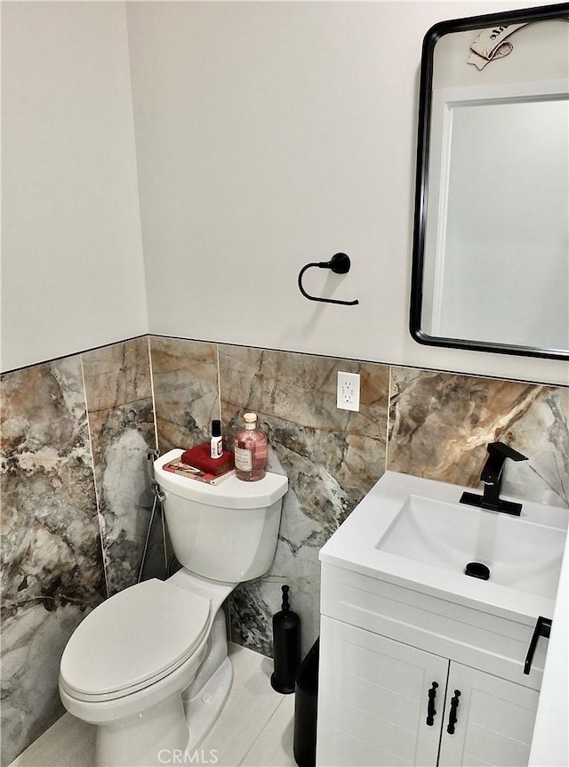 half bath with wainscoting, vanity, toilet, and tile walls