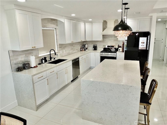 kitchen featuring a kitchen island, a sink, white cabinets, wall chimney range hood, and appliances with stainless steel finishes