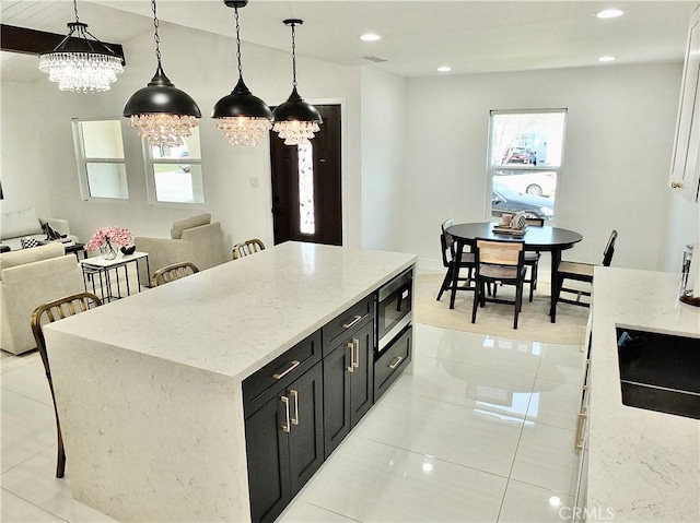 kitchen featuring open floor plan, dark cabinetry, a center island, stainless steel microwave, and pendant lighting