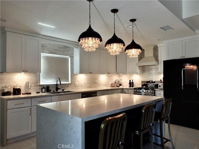 kitchen with a sink, visible vents, wall chimney range hood, black fridge, and stainless steel gas stove