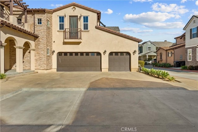 mediterranean / spanish home featuring concrete driveway, a tile roof, stucco siding, stone siding, and an attached garage