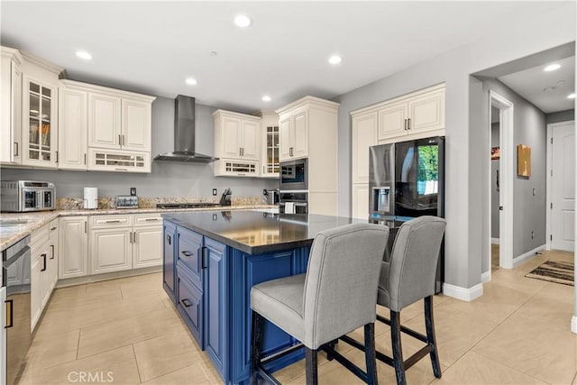 kitchen with blue cabinetry, appliances with stainless steel finishes, a kitchen breakfast bar, light tile patterned flooring, and wall chimney exhaust hood