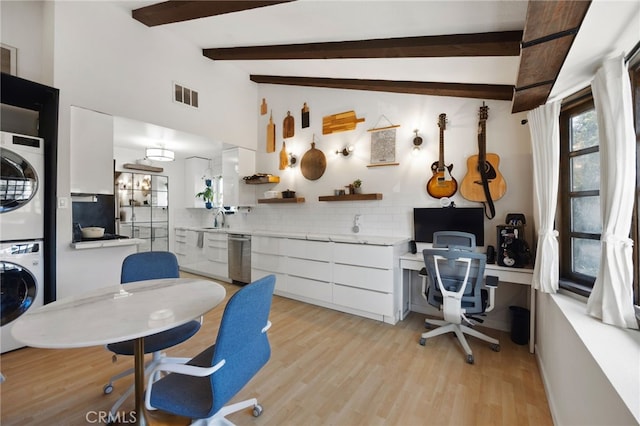 office with light wood finished floors, stacked washer / drying machine, visible vents, lofted ceiling with beams, and a sink