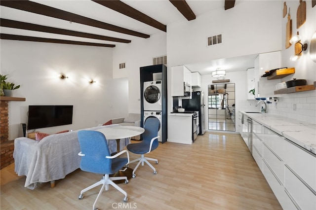 dining space with light wood-style floors, beam ceiling, visible vents, and stacked washer / drying machine