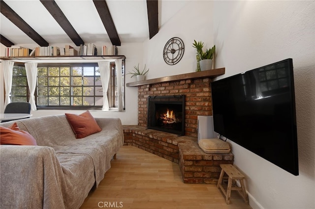 living area featuring a fireplace, beam ceiling, and wood finished floors