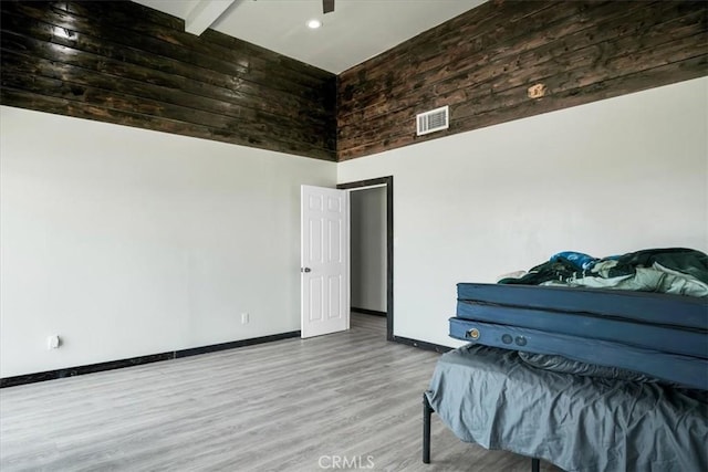 bedroom featuring beam ceiling, visible vents, a high ceiling, wood finished floors, and baseboards