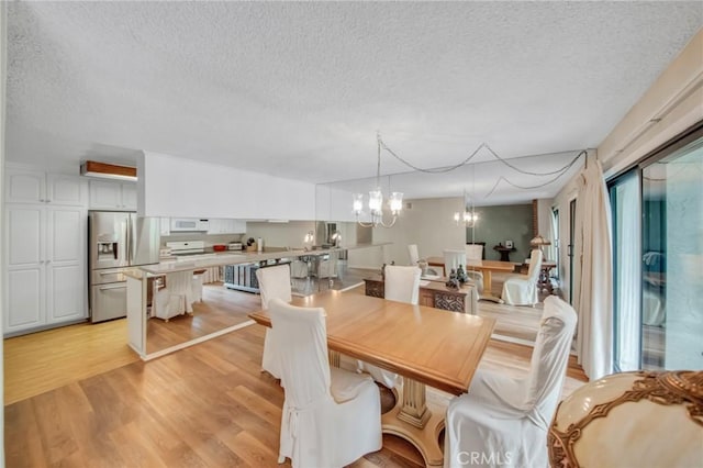 dining area featuring a notable chandelier, a textured ceiling, and light wood finished floors