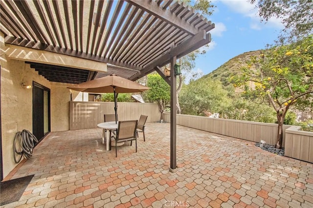 view of patio featuring outdoor dining space, fence, a mountain view, and a pergola