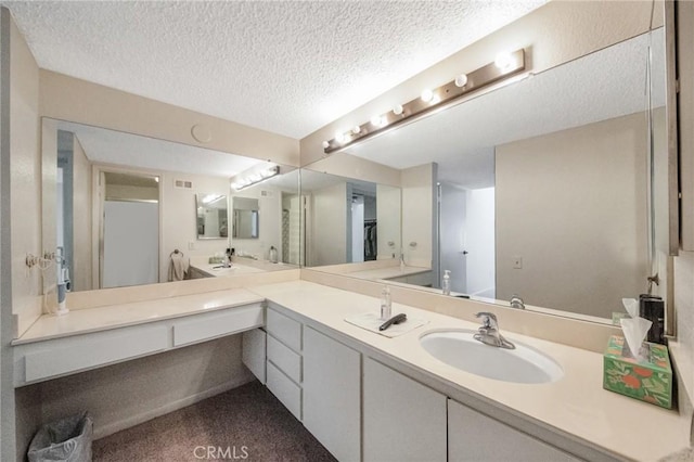 full bathroom featuring a textured ceiling, double vanity, walk in shower, and a sink