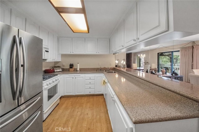 kitchen with a peninsula, white appliances, white cabinetry, light wood-style floors, and light stone countertops