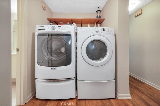 laundry area featuring a textured ceiling, laundry area, wood finished floors, baseboards, and independent washer and dryer