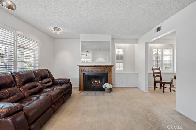 carpeted living area featuring visible vents, a fireplace with flush hearth, a textured ceiling, and baseboards