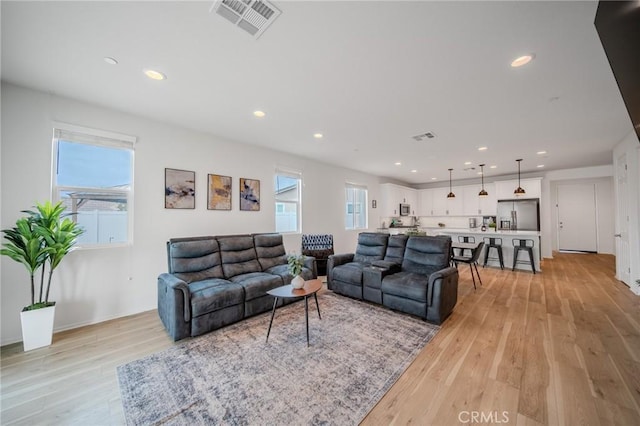 living area featuring light wood-style floors, plenty of natural light, and visible vents