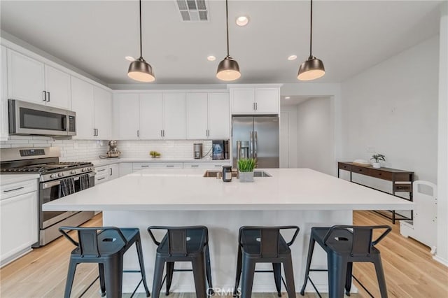 kitchen with appliances with stainless steel finishes, visible vents, decorative backsplash, and a kitchen breakfast bar