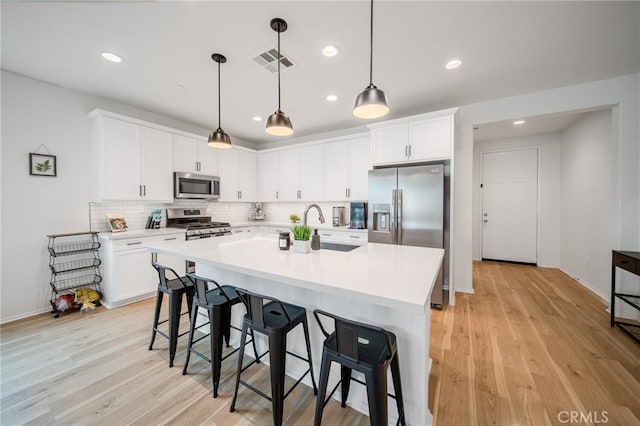 kitchen with visible vents, a breakfast bar area, appliances with stainless steel finishes, light countertops, and a sink