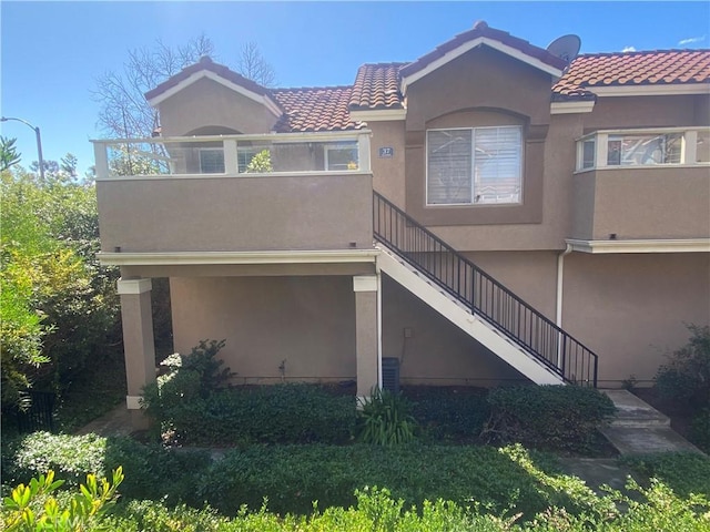 exterior space with stairs, a balcony, a tiled roof, and stucco siding