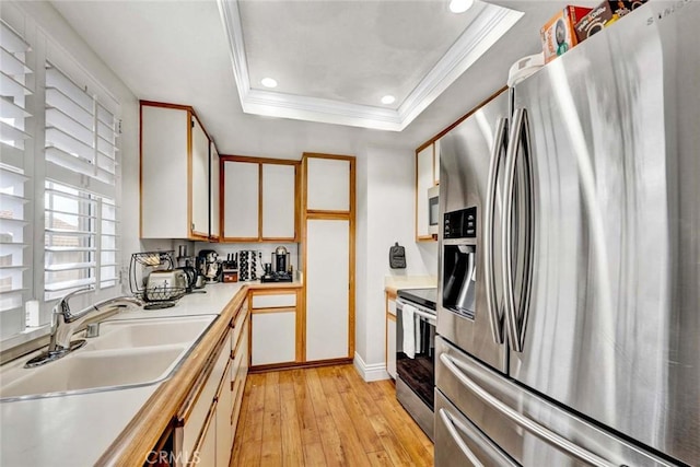 kitchen with light wood-type flooring, ornamental molding, a tray ceiling, stainless steel appliances, and light countertops