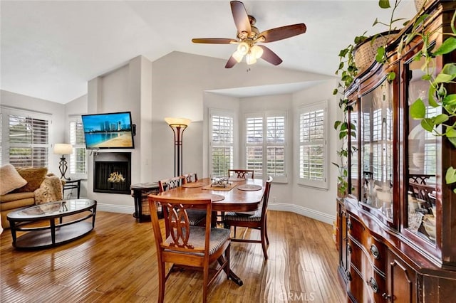 dining room featuring a wealth of natural light, a fireplace, light wood-type flooring, and vaulted ceiling