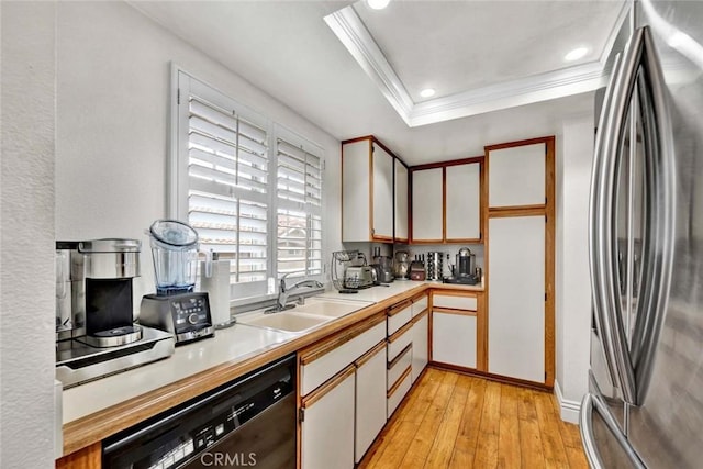 kitchen with a sink, a tray ceiling, freestanding refrigerator, light countertops, and dishwasher