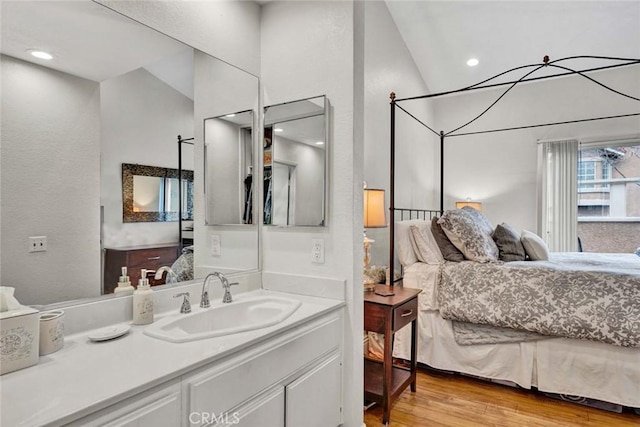 ensuite bathroom with connected bathroom, lofted ceiling, wood finished floors, and vanity