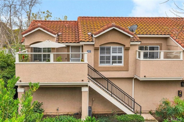 back of house featuring a tile roof, stairway, and stucco siding