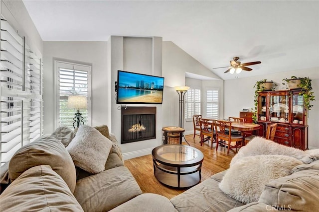 living room featuring a large fireplace, ceiling fan, baseboards, lofted ceiling, and wood finished floors