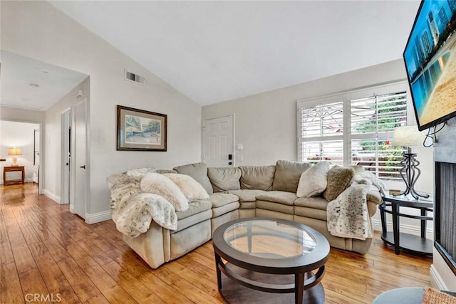 living room featuring visible vents, high vaulted ceiling, a fireplace, light wood finished floors, and baseboards