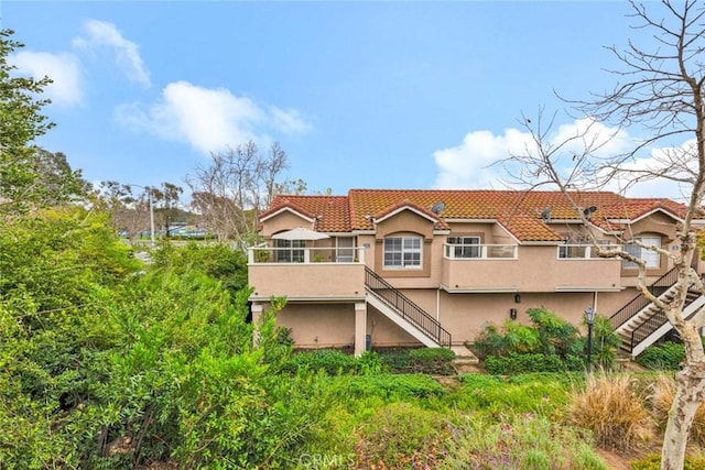 back of property featuring a tiled roof, stairway, a sunroom, and stucco siding