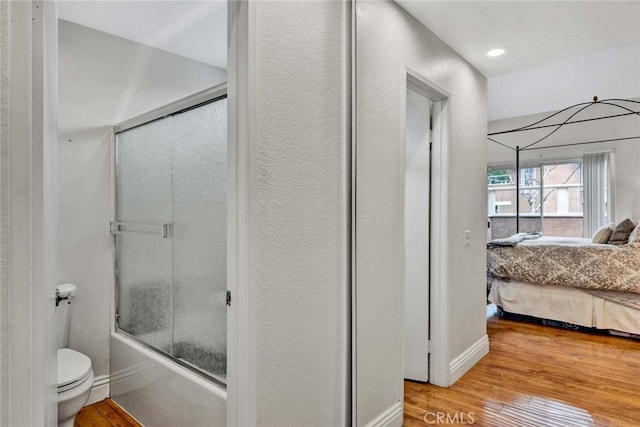 ensuite bathroom with connected bathroom, baseboards, bath / shower combo with glass door, toilet, and hardwood / wood-style floors