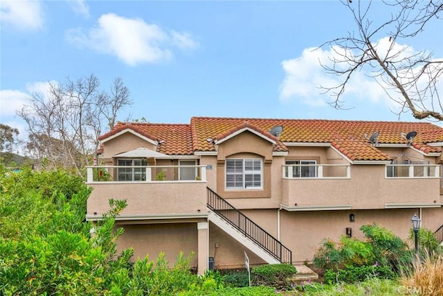 back of property featuring a tiled roof, stairway, and stucco siding